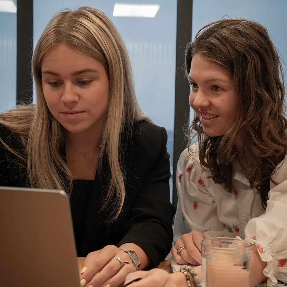 Nomi en Vera zitten achter hun laptop en bespreken samen verschillende ideeën in de vergaderruimte op het kantoor van BrandFirst