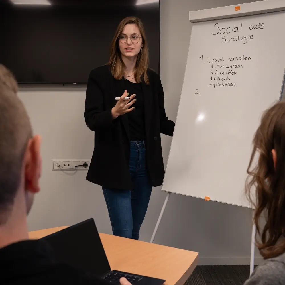 Sanne leidt een brainstorm over hoe we een social media strategie het beste in kunnen zetten. Ze beschrijft welke platformen er het beste gebruikt kunnen worden, zoals Instagram, Facebook, TikTok en Pinterest. Dit alles schrijft ze op een whiteboard.